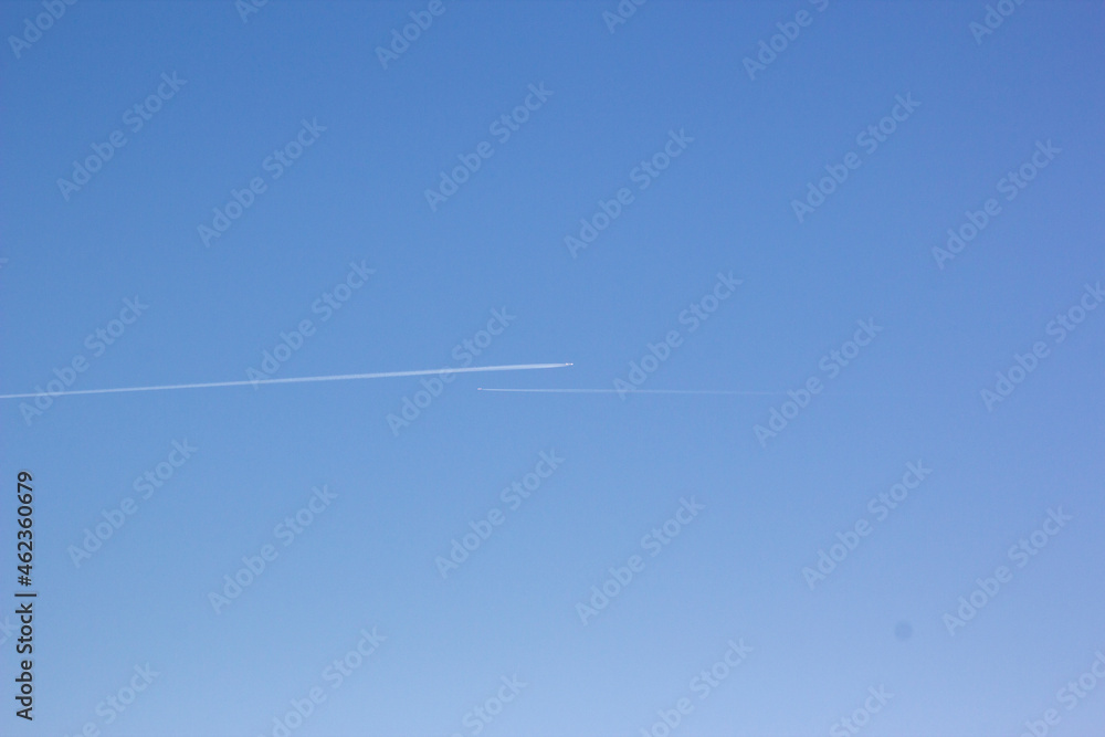 Two planes fly towards each other. Inversion trail of clouds from the plane against the blue sky. Airplane leaving vapor trail behind. Track in the sky from a jet plane. Two planes fly towards each other. Inversion trail of clouds from the plane against the blue sky. Airplane leaving vapor trail behind. Track in the sky from a jet plane.