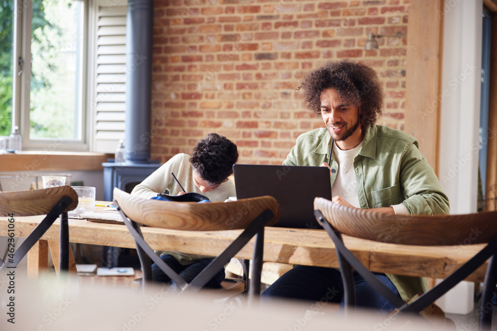 Fototapeta premium Father using laptop with son doing homework