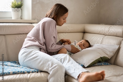 Mother measuring temperature of her ill kid at background. Sick child with high fever lying at sofa at home. High quality 4k footage