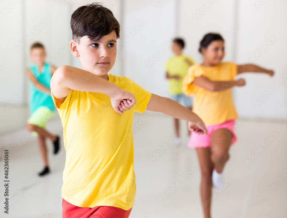 Focused preteen boy learning moves of traditional Caucasian dance lezginka during group class in children choreographic studio.