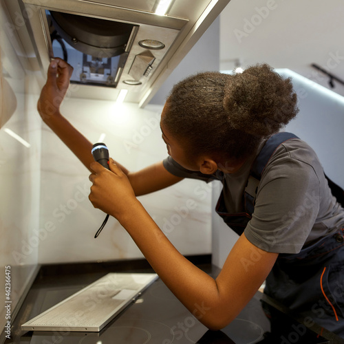 Young African American handywoman troubleshooting kitchen exhaust fan photo