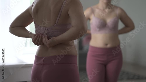 A woman tries on a bra in the fitting room, a bustier with a wide clasp is reflected in the mirror, close-up 4k video photo