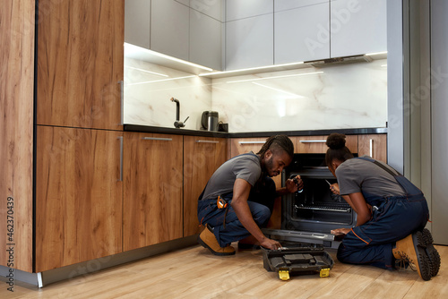 Two African American repairpersons in front of opened kitchen oven