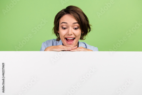 Photo of amazed positive young happy woman look empty space banner white copyspace isolated on green color background