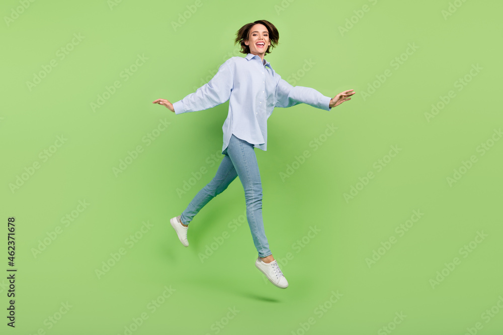 Full length photo of cheerful positive nice happy woman jump up walk empty space isolated on green color background Full length photo of cheerful positive nice happy woman jump up walk empty space isolated on green color background