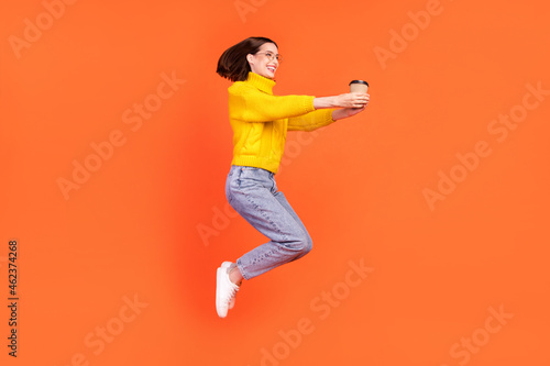 Fototapeta Naklejka Na Ścianę i Meble -  Full body profile side photo of young woman happy positive smile give cup of coffee jump up isolated over orange color background