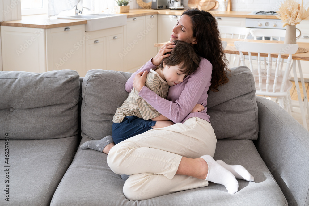 Affectionate mother parent caring embrace little son expressing family connection and tenderness. Loving mom comfort small boy with tender hug sitting on sofa at home. Mum and kid relationship concept