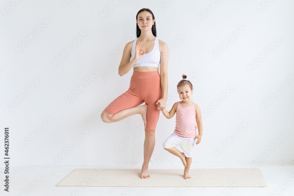 Young woman practices yoga with her daughter. Children's yoga. Vrikshasana pose.