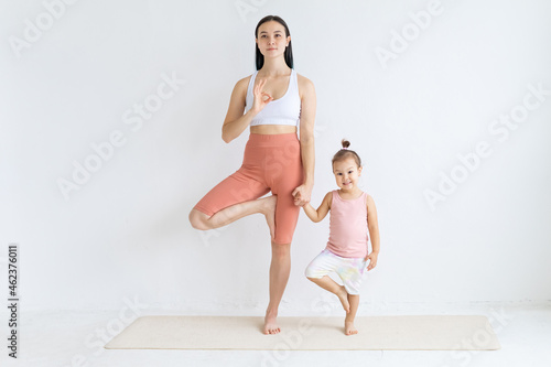 Young woman practices yoga with her daughter. Children's yoga. Vrikshasana pose.