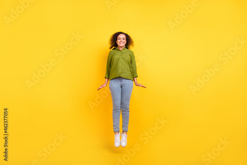 Photo of funky positive charming pretty woman dressed green shirt jumping high smiling isolated yellow color background