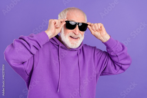 Portrait of attractive cheerful grey-haired man touching specs good mood isolated over bright violet purple color background © deagreez