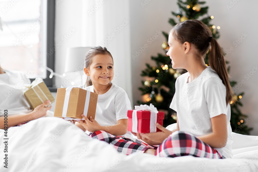 family, winter holidays and people concept - happy mother, father and two daughters in pajamas with christmas gifts in bed at home