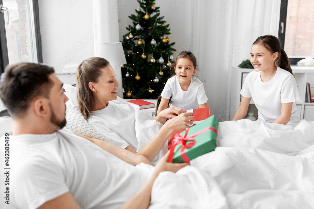 family, winter holidays and people concept - happy mother, father and two daughters in pajamas with christmas gifts in bed at home family, winter holidays and people concept - happy mother, father and two daughters in pajamas with christmas gifts in bed at home