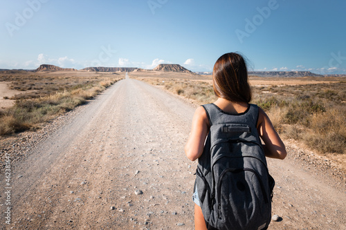 Young caucasian woman with a grey backpack walking in the middle of a dessert at Bardenas, Navarre, Basque Country.