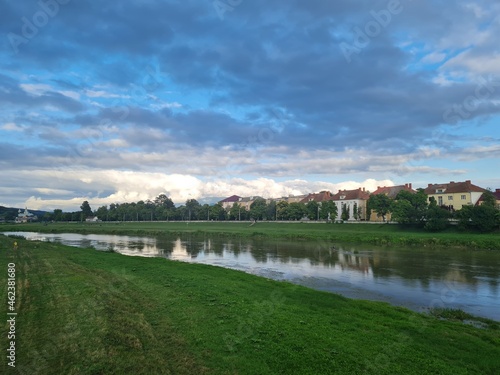 Natural beauty of blue sky and calm water of river in Mukachevo, Ukraine. Beautiful landscape with river and houses at sunset. Scenic view of the old town embankment on a cloudy summer day at dusk.