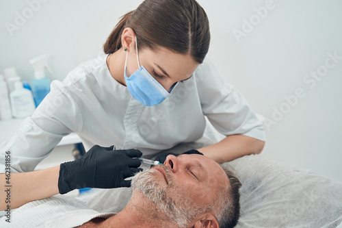 Doctor cosmetologist making injection into man face