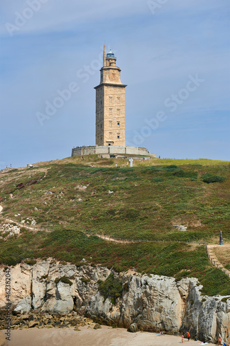 the tower of hercules can be seen at the top of the hill above the cliffs overlooking the beach © Javi