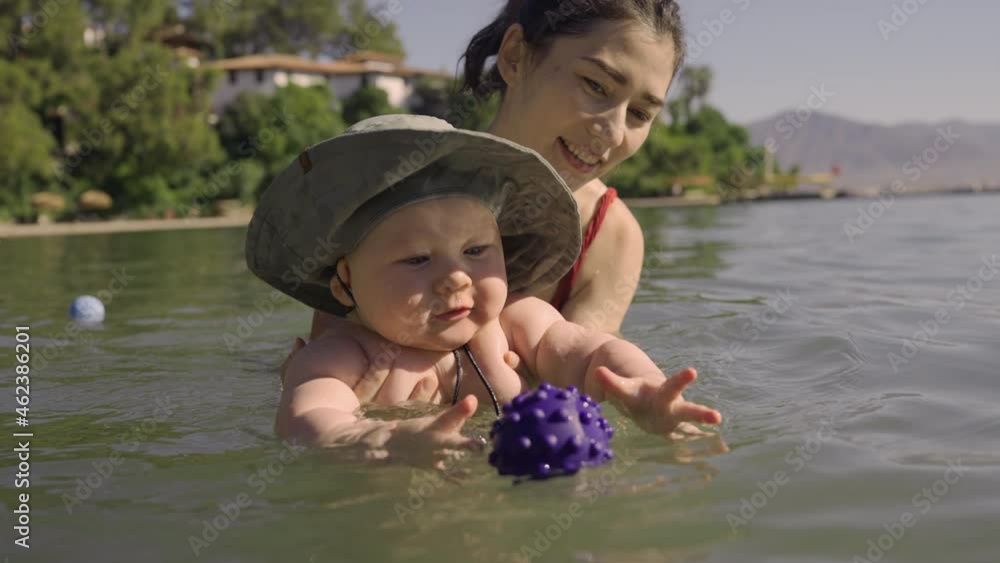 Happy young mom throws up baby in the pool. The development of kids. Bright light is shines from the windows of the indoors swimming pool. Slow motion Happy young mom throws up baby in the pool. The development of kids. Bright light is shines from the windows of the indoors swimming pool. Slow motion