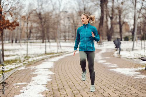 Fit sportswoman jogging on path in park on snowy winter day. Recreation, snowy weather, winter day