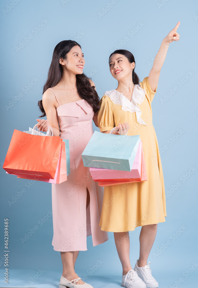 Two young Asian women holding shopping bag on blue background Two young Asian women holding shopping bag on blue background