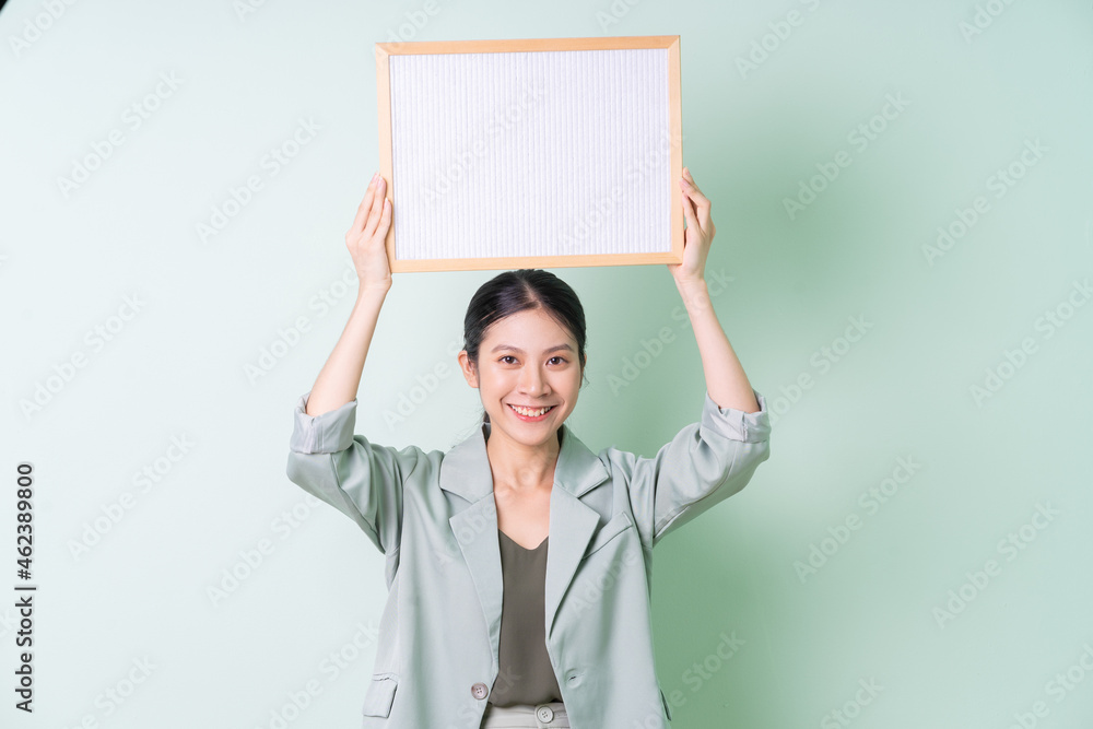 Young Asian businesswoman holding white board on green background Young Asian businesswoman holding white board on green background