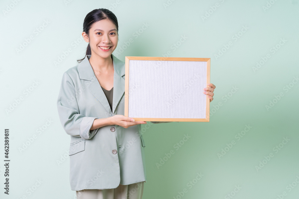 Young Asian businesswoman holding white board on green background Young Asian businesswoman holding white board on green background
