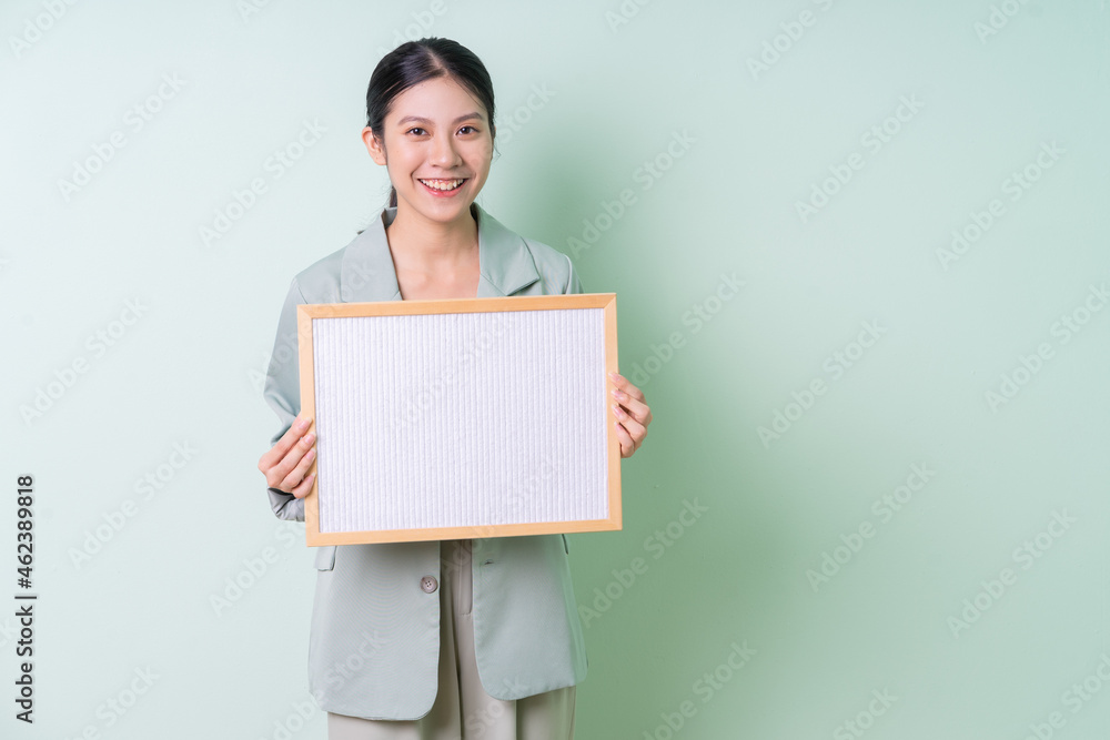 Young Asian businesswoman holding white board on green background Young Asian businesswoman holding white board on green background