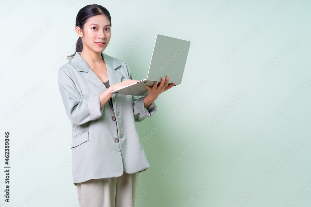 Young Asian businesswoman holding laptop on green background Young Asian businesswoman holding laptop on green background