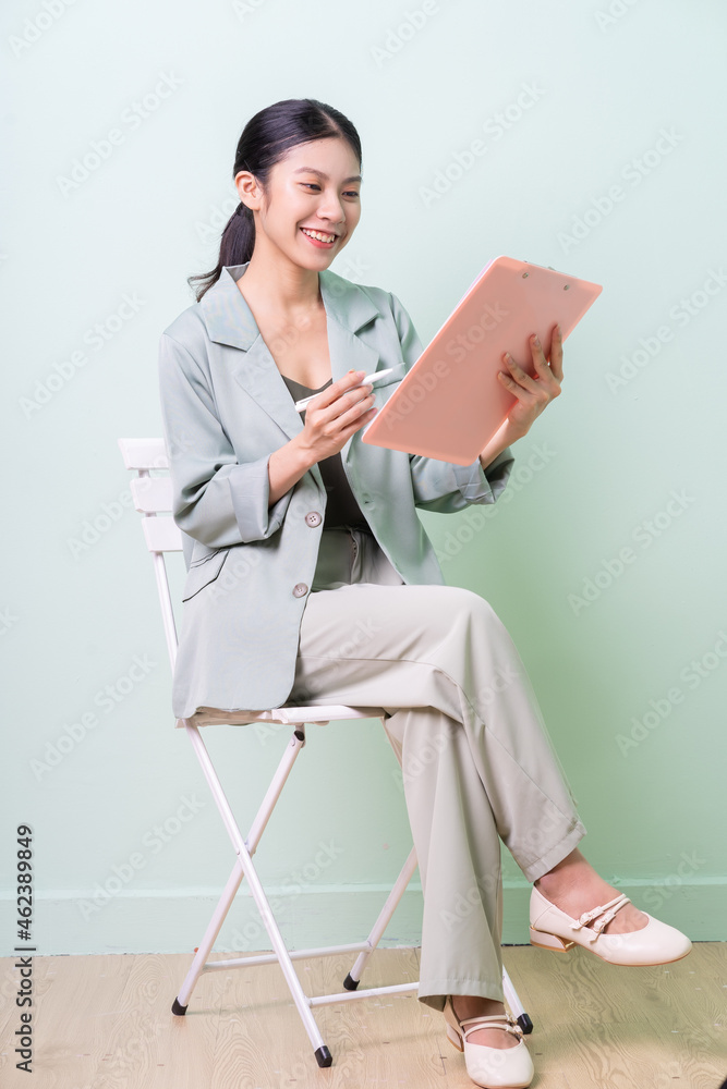 Young Asian businesswoman sitting on chair on green background Young Asian businesswoman sitting on chair on green background
