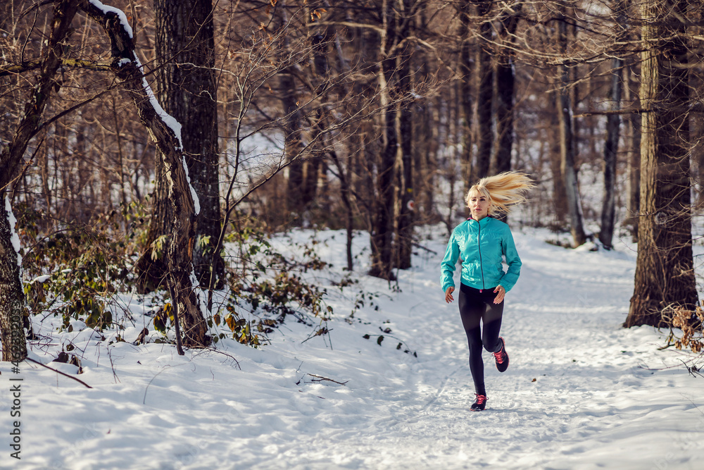 Fit sportswoman jogging on snowy path in forest at winter. Healthy lifestyle, winter fitness