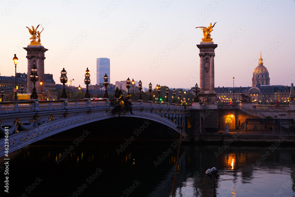 Early morning view of famous Alexandre III bridge across Seine river in Paris and golden dome of Hotel of Invalides ..