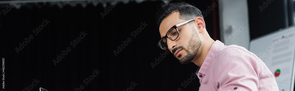 Young arabian businessman in eyeglasses looking away in office, banner Young arabian businessman in eyeglasses looking away in office, banner