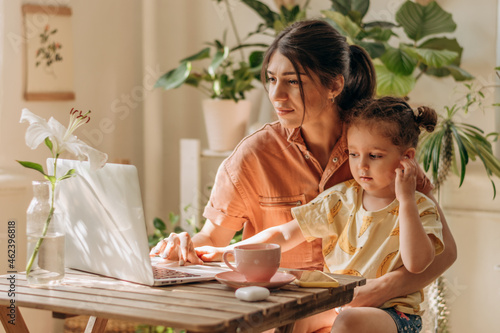 Tired businesswoman young woman of mixed race with her little daughter is using a laptop at home office.Child distracts mom from work.Remote work at home, freelance, working moms,online education.