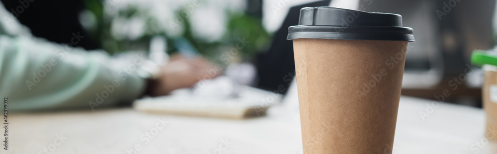 Cropped view of coffee to go near blurred businessman in office, banner