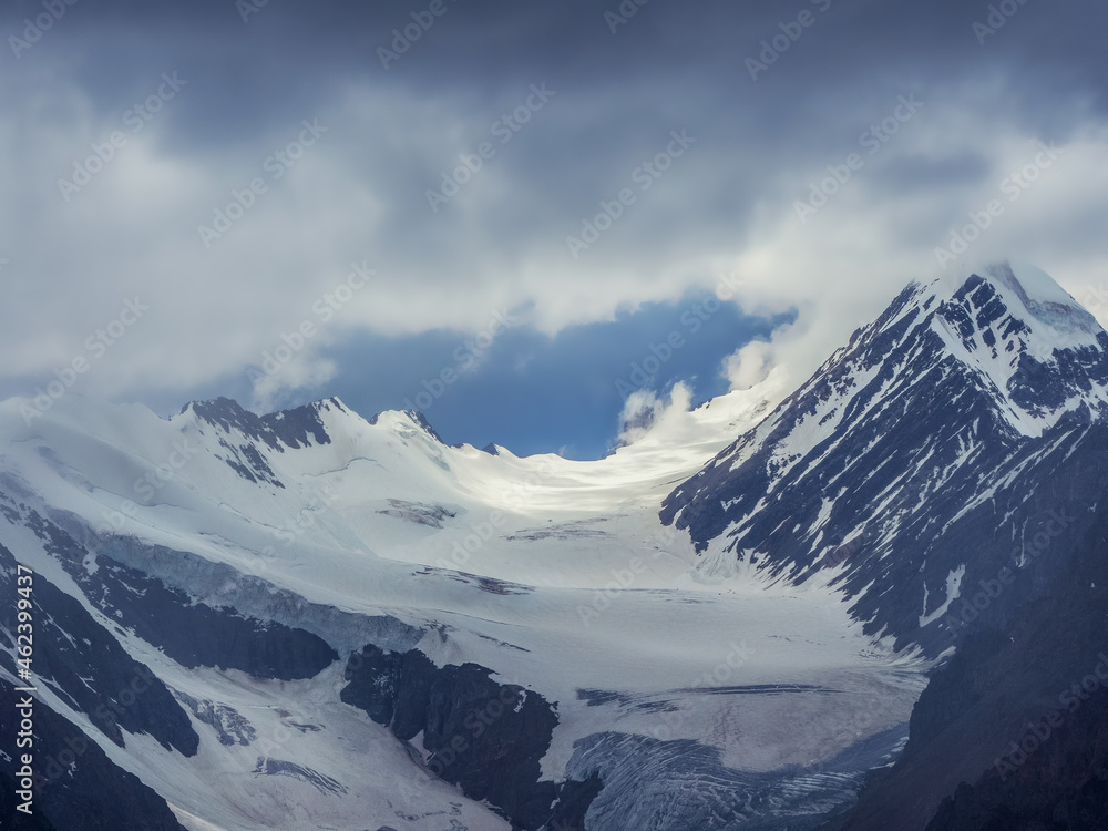 Soft focus. Wonderful minimalist landscape with big snowy mountain peaks above low clouds. Atmospheric minimalism with large snow mountain tops, dark glacier in cloudy sky.
