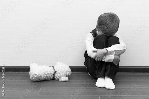 Foto A little boy of six is offended and sits on the floor against a white wall next to a soft toy with his hands closed