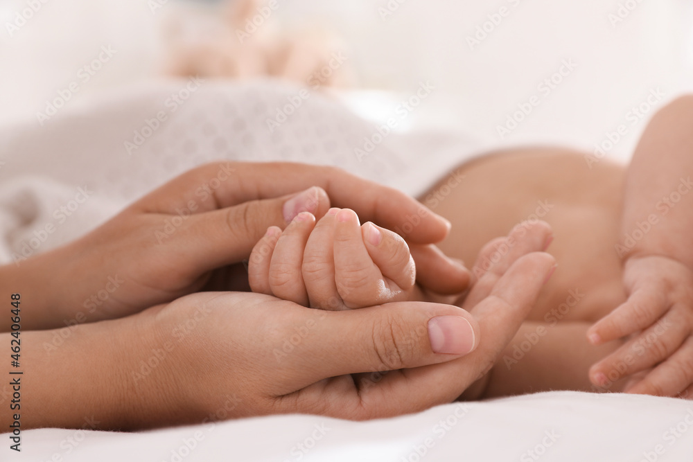 Mother with her cute baby on bed at home, closeup of hands Mother with her cute baby on bed at home, closeup of hands