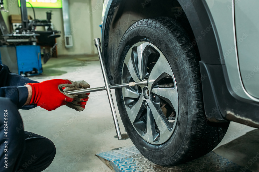 car service, the car is on a lift, the worker removes / installs the wheel, he has a tool in his hands