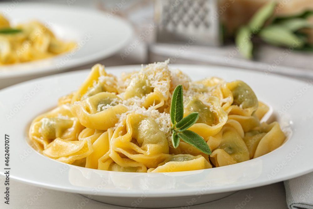Close-up of tortelloni stuffed with spinach and ricotta, stir-fried with melted butter and sage leaves. Grated parmesan cheese. Close-up of tortelloni stuffed with spinach and ricotta, stir-fried with melted butter and sage leaves. Grated parmesan cheese.