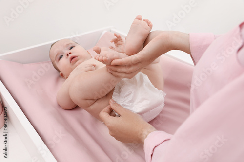 Mother changing baby's diaper at home, focus on hands