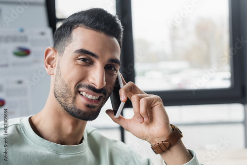 Smiling muslim businessman talking on smartphone and looking at camera in office