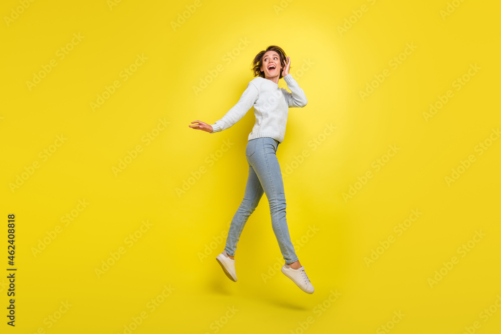 Photo of crazy shocked funny lady jump look empty space wear blue sweater jeans footwear isolated yellow color background