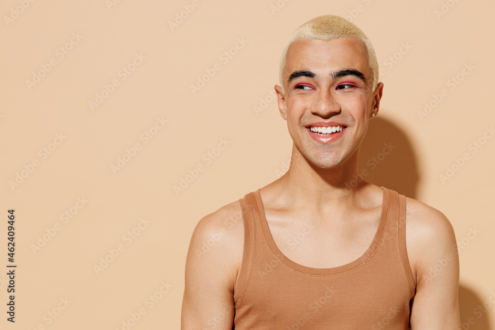 Young smiling laughing cheerful blond latin american gay man 20s with make up in beige tank shirt looking aside isolated on plain light ocher background studio portrait People lgbt lifestyle concept - obrazy, fototapety, plakaty 
