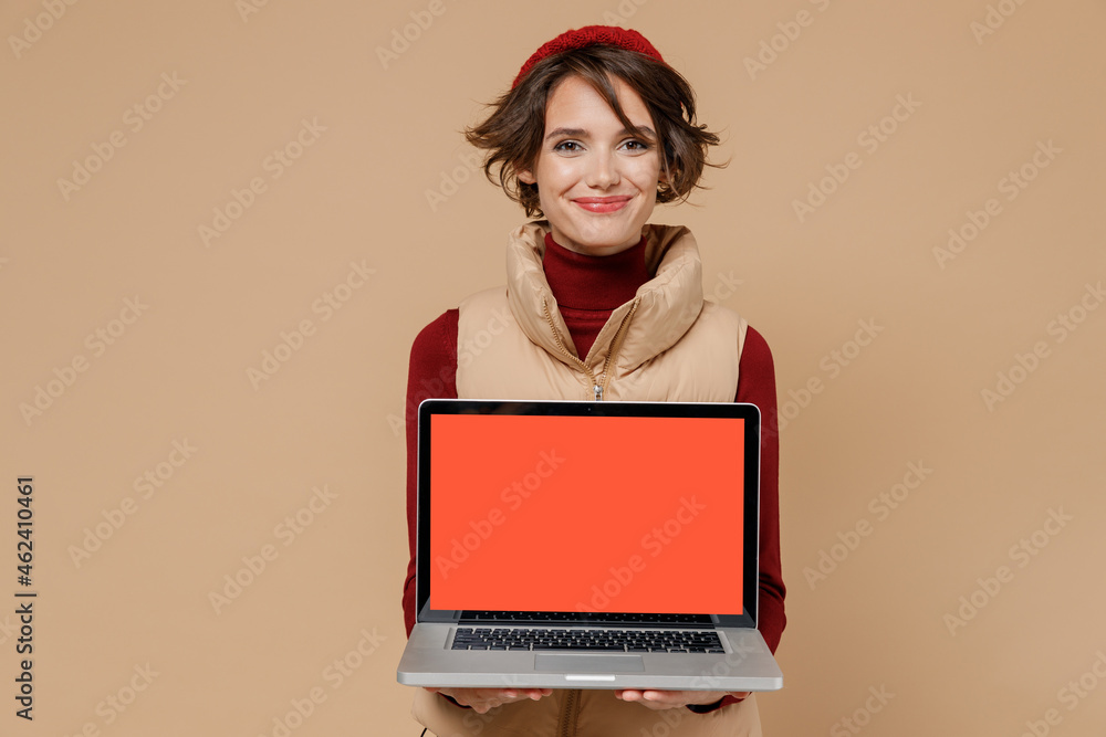 Naklejka premium Young smiling happy cheerful woman 20s wears red turtleneck vest beret hold use work on laptop pc computer with blank screen workspace area isolated on plain pastel beige background studio portrait