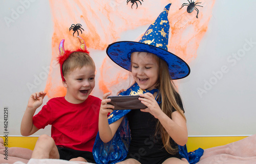 children dressed in Halloween costumes, girls in hats are video chatting on the phone with friends in a decorated house. A traditional autumn holiday. Halloween concept, magic, holidays and mystical