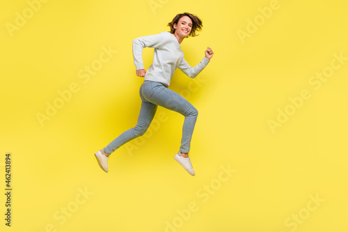Full length profile photo of funny millennial brunette lady run wear pullover jeans sneakers isolated on yellow background