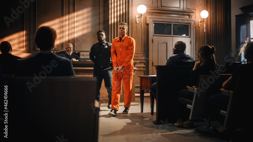 Foto Cinematic Court of Law and Justice Trial Proceedings: Portrait of Accused Sad Male Criminal in Orange Jumpsuit Led Away by Security Guard in Front of Judge and Jury