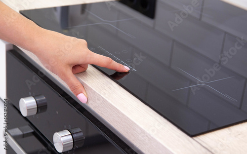 Modern induction ceramic hob with 4 cooking zones. Woman presses hand on touch control display, close-up photo