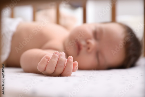 Fotografie Cute little baby sleeping in crib at home, focus on hand. Bedtime