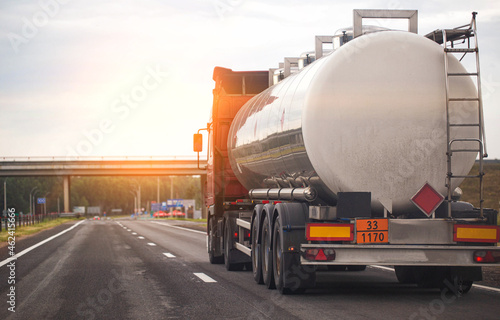 A truck with a tank trailer transports a liquid dangerous cargo on a highway against the backdrop of a sunset. Copy space for text